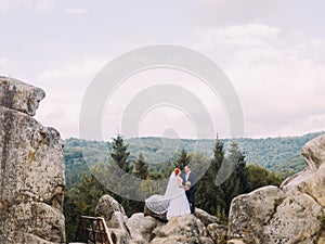 Wedding couple standing at rocky mountains against the sky. Cute romantic moment.