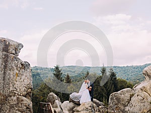 Wedding couple standing at rocky mountains against the sky and kissing. Cute romantic moment.