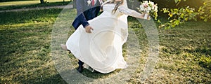 Wedding couple walking in the green park. Curvy bride in white lace dress and groom are holding hands. Overweight happy people.