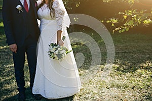 Wedding couple walking in the green park. Curvy bride in white lace dress and groom are holding hands. Overweight happy people.