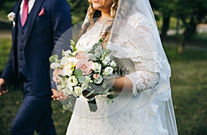 Wedding couple walking in the green park. Curvy bride in white lace dress and groom are holding hands. Overweight happy people.