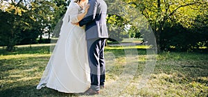 Wedding couple walking in the green park. Curvy bride in white lace dress and groom are holding hands. Overweight happy people.