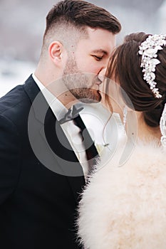 Wedding couple in winter time walking outside. Handsome bearded groom kiss beautiful bride