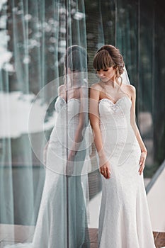 Wedding day. Bride portrait in white dress by the window outside. Beauty portrait of bride wearing fashion wedding dress