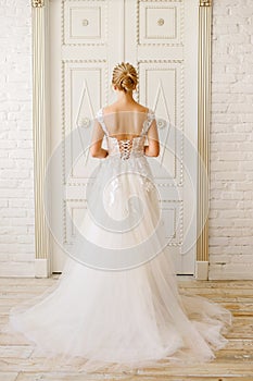 Wedding day, the bride in a white long dress stands near a large wooden door, vertical photo