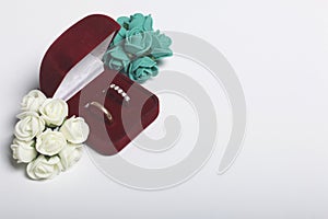 Wedding decor. Bouquet of artificial flowers and wedding rings in box lie on a white surface.