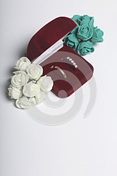 Wedding decor. Bouquet of artificial flowers and wedding rings in box lie on a white surface.