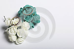 Wedding decor. Bouquet of artificial flowers and wedding rings lie on a white surface.