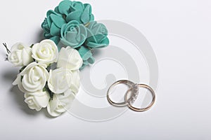 Wedding decor. Bouquet of artificial flowers and wedding rings lie on a white surface.