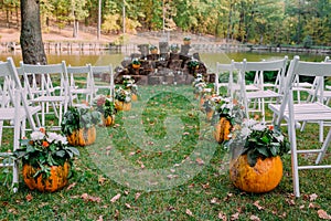 Wedding decoration with autumn pumpkins and flowers. Ceremony outdoor in the park. White chairs for guests