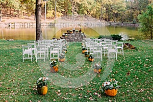 Wedding decoration with autumn pumpkins and flowers. Ceremony outdoor in the park. White chairs for guests