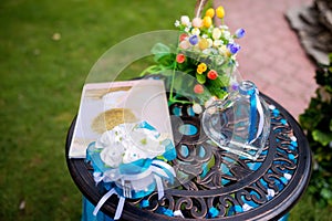 Wedding decoration details. Heart - shaped glass bottle with blue ribbon on a metal table. Closeup.