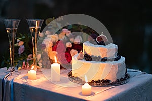 Wedding decorations. cake in white glaze with a decor of blueberries and figs on the table in the evening with glasses, lit