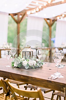 Wedding decorations in rustic style on wooden table, flower arrangement and golden lantern. Table served with cutlery