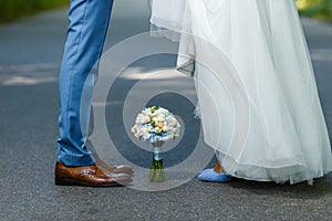 Wedding details: classic brown and blue shoes of bride and groom. Bouquet of roses standing on the ground between them. Newlyweds