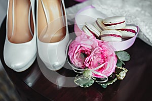 Wedding details, decoration. Bouquet of pink roses, bridal accessories and macaroons stand on a wooden table. Soft focus