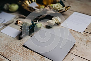 Wedding details, invitations, craft envelopes, groom boutonniere, rings, flowers, vase on a white wooden background