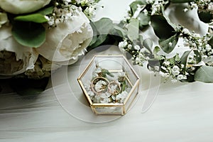 Wedding details. two classic gold wedding rings in a glass box and a bouquet of white flowers and greenery