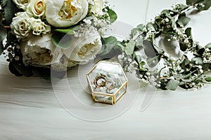 Wedding details. two classic gold wedding rings in a glass box and a bouquet of white flowers and greenery