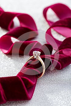Wedding diamond ring on white glossy background with burgundy ribbon