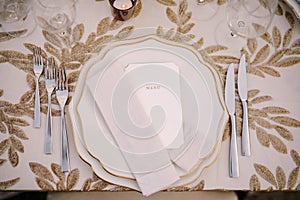 Wedding dinner table reception. Delicate creamy pastel tones of tablecloths and plates on table, three forks left and