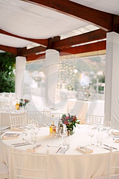 Wedding dinner table reception. Round tables with white tablecloths and white Chiavary chairs under a large white tent