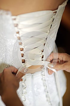 Wedding dress corset close up. Preparation of the bride. Bridesmaid tying bow on wedding dress. Bride in the white dress.