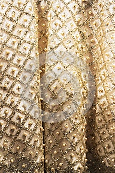 Wedding dress fabric texture background. Golden and ivory silk dress with beads, pearls, sparkles and embroidery. Vintage dress