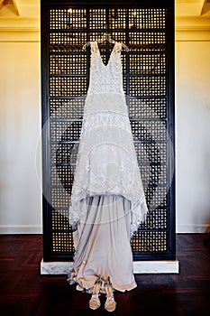 Wedding dress hanging on the wall with shoes on the floor, tungsten light in background