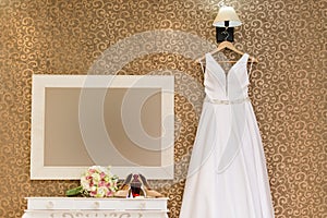 Wedding dress hanging on wall with texture and bouque, perfume and jewelry