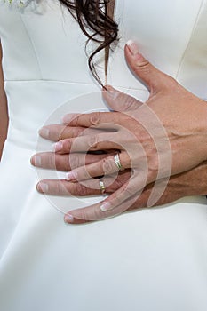 Wedding finger rings on bride groom hands on white dress background