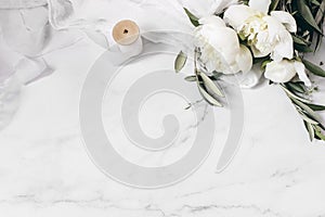 Wedding floral still life composition. Bouquet of white peony flowers, olive branches on marble table with silk cloth