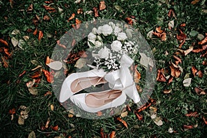 A wedding gentle bouquet of white and pink roses and high-heeled shoes on a green grass in the park. Wedding details
