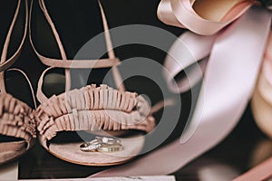 The wedding gold rings with diamonds lie on velvet pink bride shoes with satin ribbons. Close-up