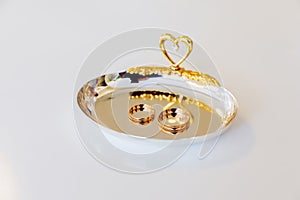 Wedding gold rings are lying on a yellow plate with a heart for a wedding