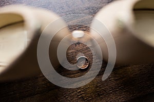 Wedding golden ring in focus lie on the wooden background another wedding ring between the bride`s shoes.