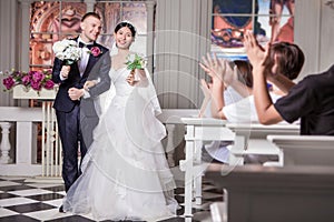 Wedding guests applauding for newlywed couple holding flowers in church