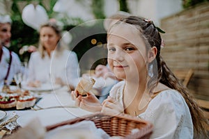 Wedding guests sitting by table, eating and drinking at reception outside in the backyard.