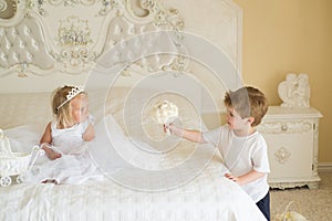 Wedding hair trends. Little flower girl wear tiara and hairstyle. Page boy with blond hair hold wedding bunch. Little