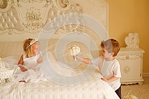 Wedding hair trends. Little flower girl wear tiara and hairstyle. Page boy with blond hair hold wedding bunch. Little