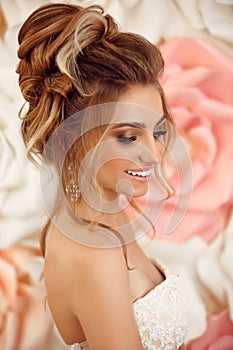 Wedding hairstyle. Attractive young bride with makeup and fashion. Closeup portrait of young gorgeous woman over roses wall