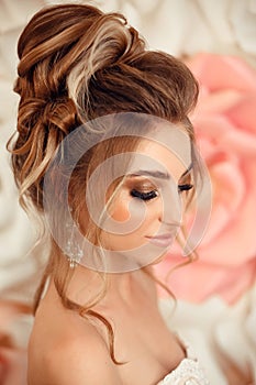 Wedding hairstyle. Attractive young bride with makeup and fashion. Closeup portrait of young gorgeous woman over roses wall