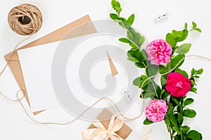 Wedding invitation card, blank paper card, craft envelope, ribbon and bouquet of pink rose flowers on white background. Minimal