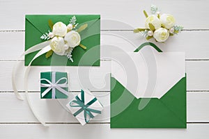 Wedding invitation cards or Valentines Day etters in green envelopes decorated with white rose flowers and two gift boxes. Flat la