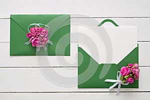 Wedding invitation cards or Valentines Day letters in green envelopes decorated with pink rose flowers. Flat lay. Top view.