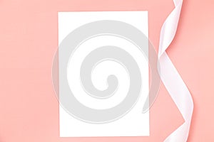 Wedding invitation or greeting card mockup with a white satin ribbon on a pink background