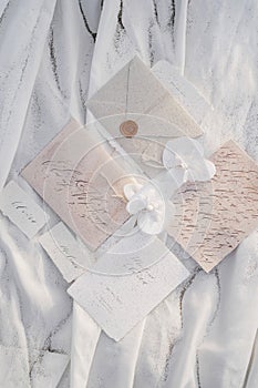 Wedding invitations with name cards lie next to envelopes and boutonnieres with beads on white fabric