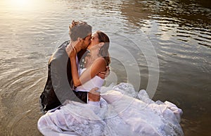 Wedding, kiss and couple in the water of a lake to celebrate their sunset marriage outdoor in nature. Happy, love and
