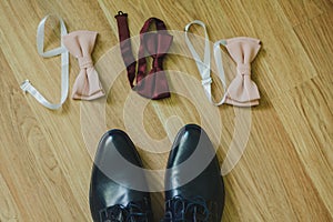 Wedding men shoes are standing near the three tie bows. Marsala dark red and nude pink colours on wooden background. Suit details