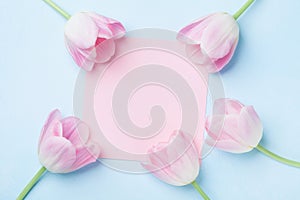 Wedding mockup with pink paper list and tulip flowers on blue table top view. Beautiful floral pattern. Flat lay style.